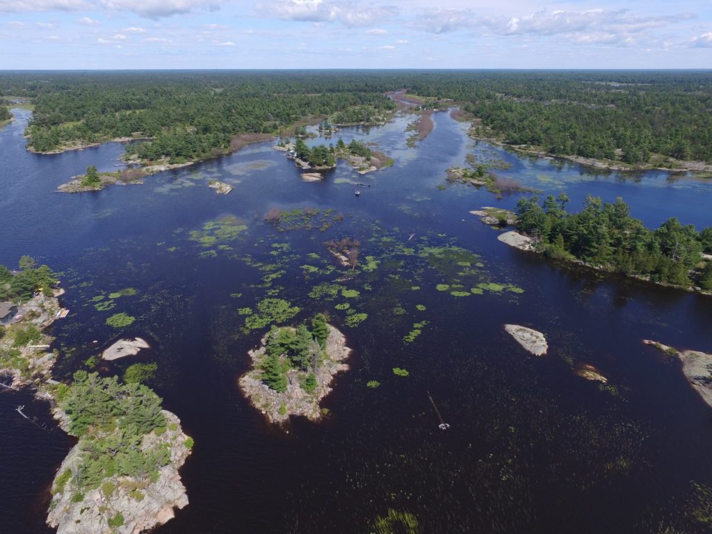 Aerial drone photo showing a water of Georgian Bay with several small islands. Some islands are small with no vegetation; others have trees on them.