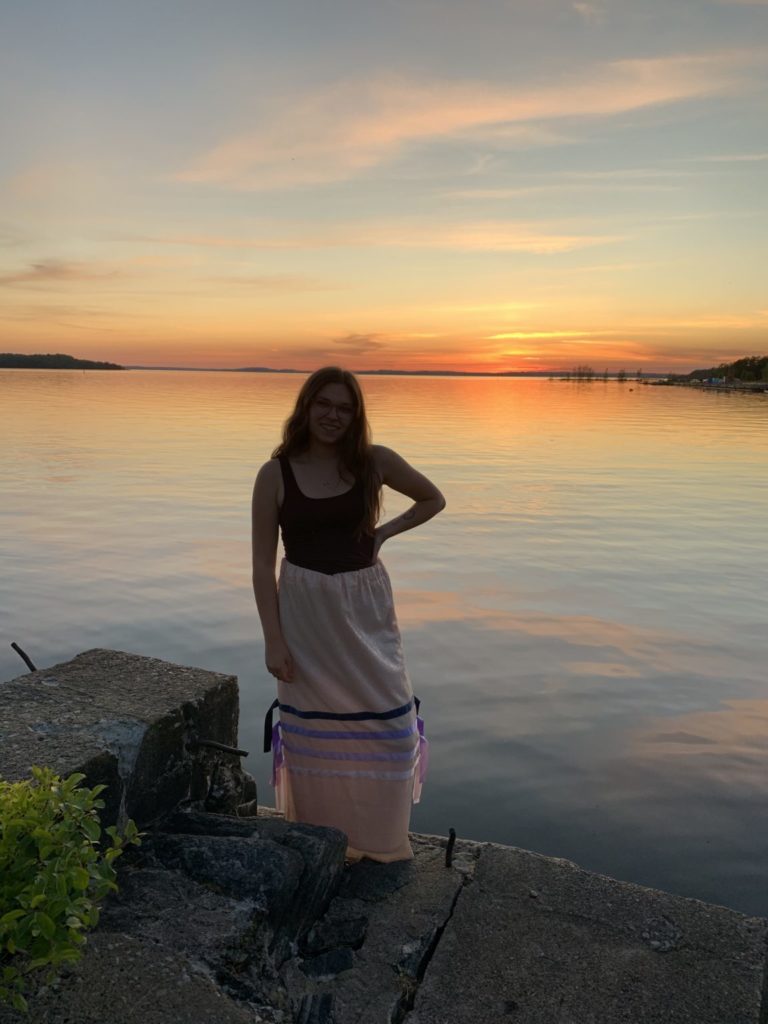 A photo of the author, Gracie Crafts, standing along the shore at sunset.